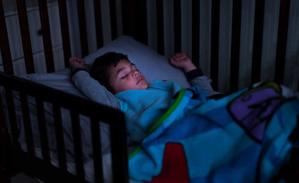 Toddler boy with his arms up by his head sleeps is his own bed 
