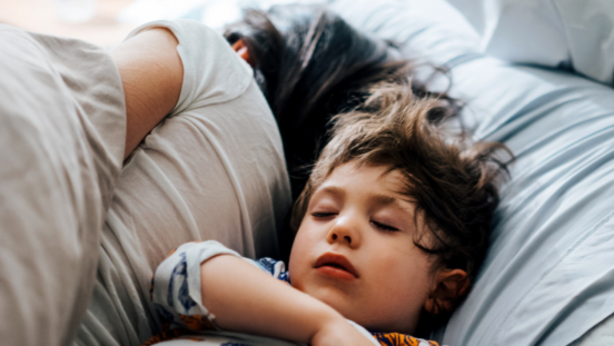 Toddler with scruffy hair sleeping peacefully next to his mum's back