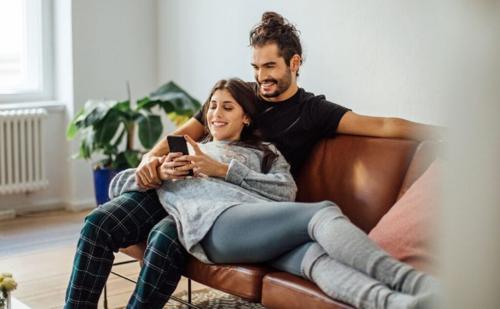 Dark hair couple lying on a couch together smiling and looking at a phone