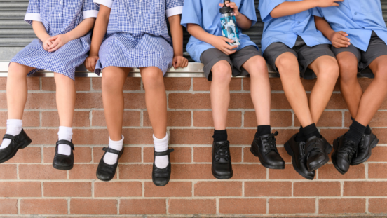 Children in school uniform sitting on a wall, heads not visible