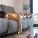 Boy laying on lounge looking bored with building blocks on the floor