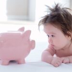 Wealthy baby names: baby boy looking at piggy bank