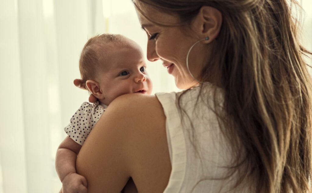 Mother smiling at newborn baby over her shoulder