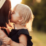 Closeup portrait of mother and little daughter playing together in summer park on sunset lights.