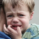 Upset little boy getting a hug as he looks over carer's shoulder.