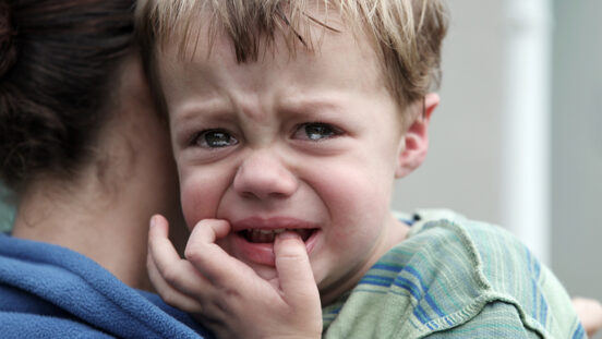 Upset little boy getting a hug as he looks over carer's shoulder.