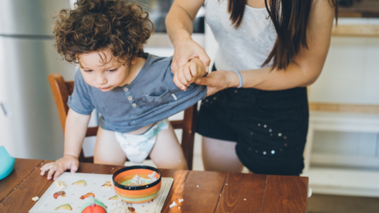 Curly haired toddler standing on dining chair