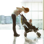 Woman at airport leaning over back of travel stroller to talk to toddler