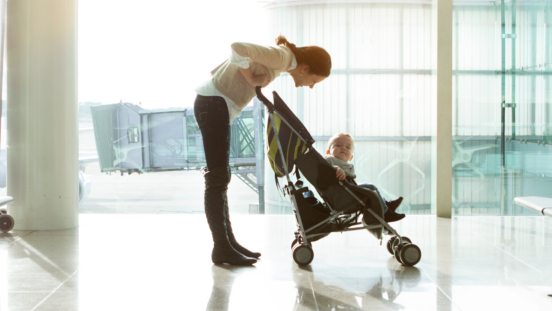 Woman at airport leaning over back of travel stroller to talk to toddler