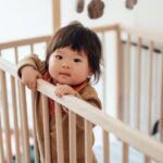 Smiling Asian baby girl standing in cot