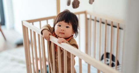 Smiling Asian baby girl standing in cot