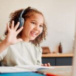 Young girl wearing headphones, waving as she does online gaming
