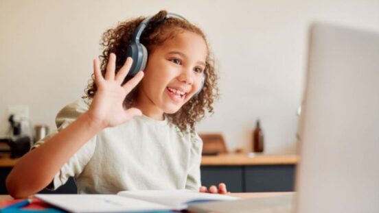 Young girl wearing headphones, waving as she does online gaming