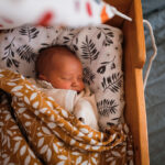 Wrapped newborn baby sleeps in wooden hanging retro cradle with muslin