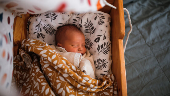 Wrapped newborn baby sleeps in wooden hanging retro cradle with muslin