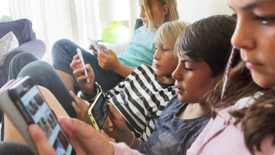 Four children sat on sofa looking at phones and tablets