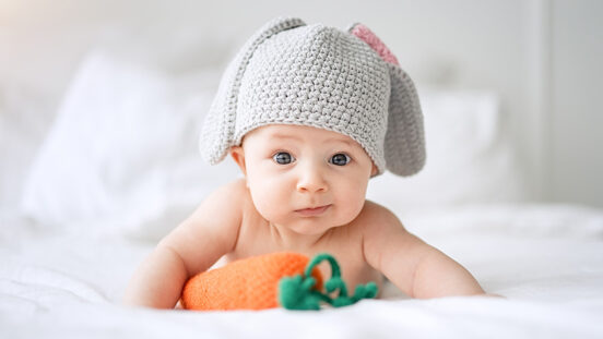 Happy child with bunny ears beannie and lying on a bed with a knitted toy carrot