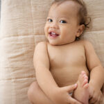 Smiling child lying back on bed holding feet