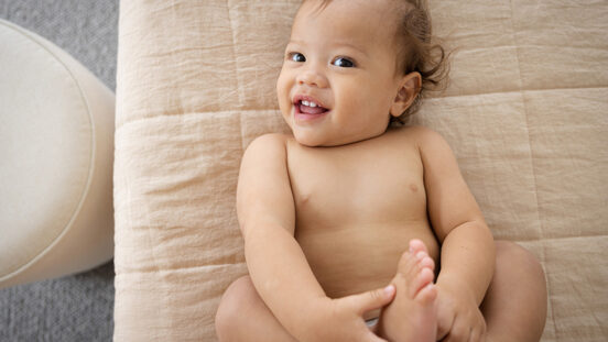 Smiling child lying back on bed holding feet