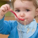 Baby boy wearing bandanna baby bib and eating with a spoon