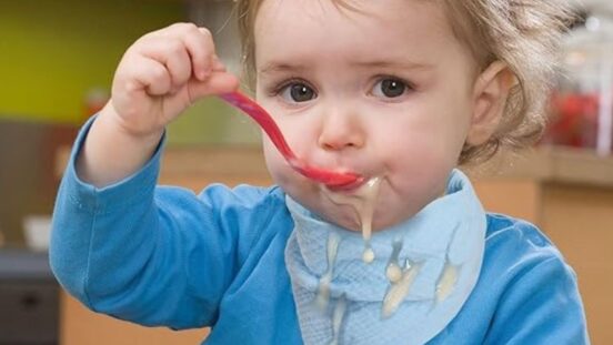 Baby boy wearing bandanna baby bib and eating with a spoon