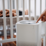 Hand turning on an air purifier with a baby's cot in the background
