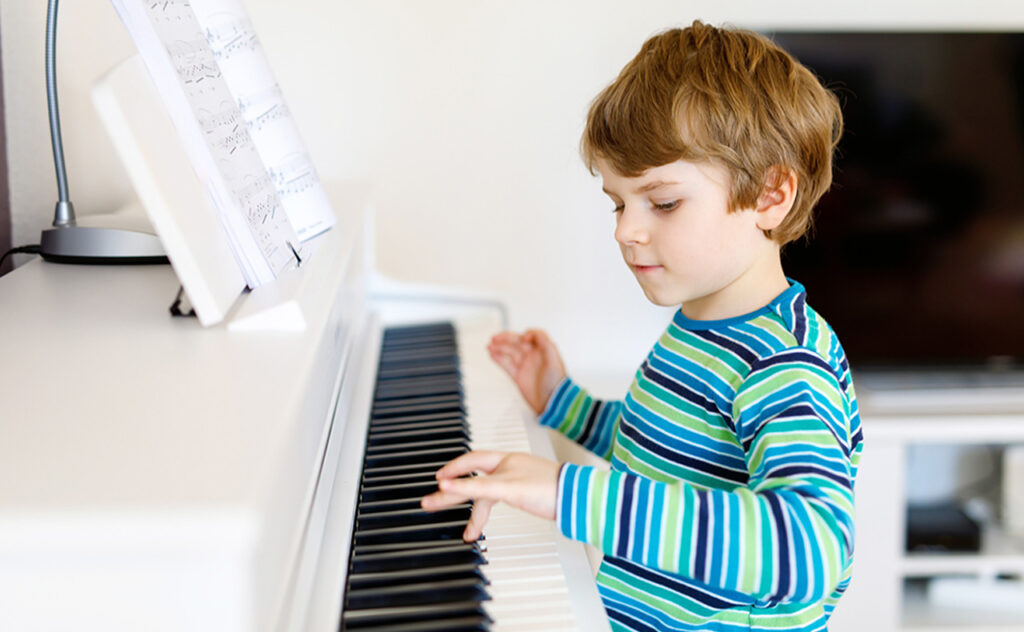 Beautiful little kid boy playing piano in living room or music school. Preschool child having fun with learning to play music instrument. Education, skills concept.
