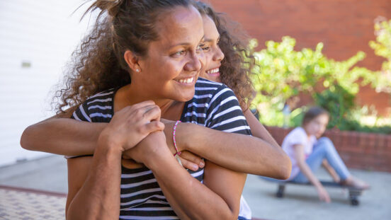 mothers day gift ideas - Mother and daughter with curly hair embracing at home in Australia