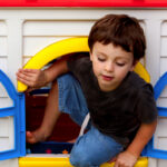 Boy plays and climbs through plastic window of toy cubby house.