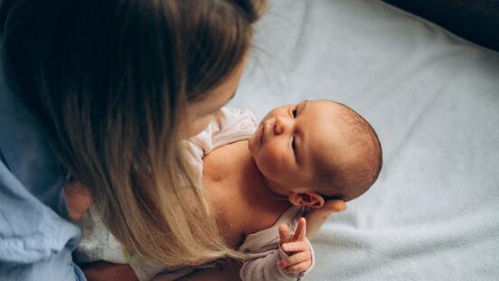 Mother making eye contact with alert newborn as she gets them dressed.