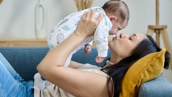 Woman holding and kissing her baby while lying on the sofa.