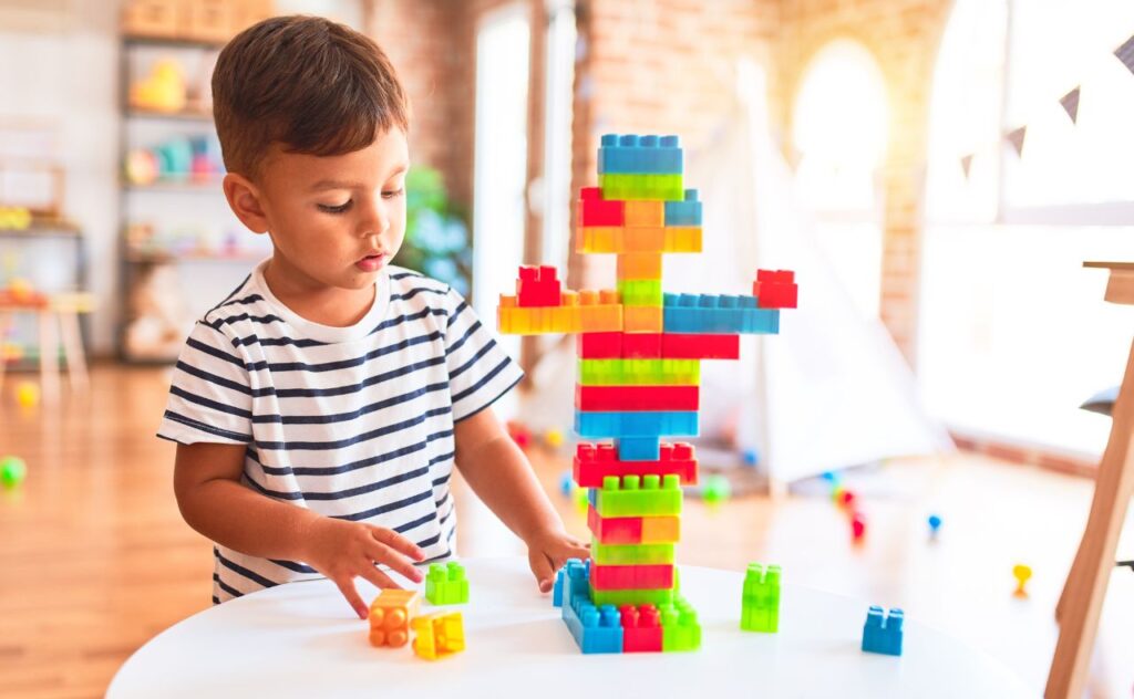 Beautiful toddler boy playing with construction blocks at kindergarten