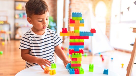 Beautiful toddler boy playing with construction blocks at kindergarten