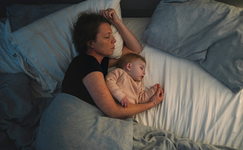 A mature mother asleep with her baby girl. The warm light from the sidelight washes over them