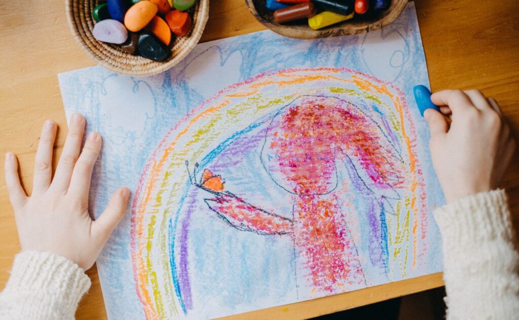 Colourful kid's crayon drawing of a rainbow and a person holding an orange butterfly on their hand