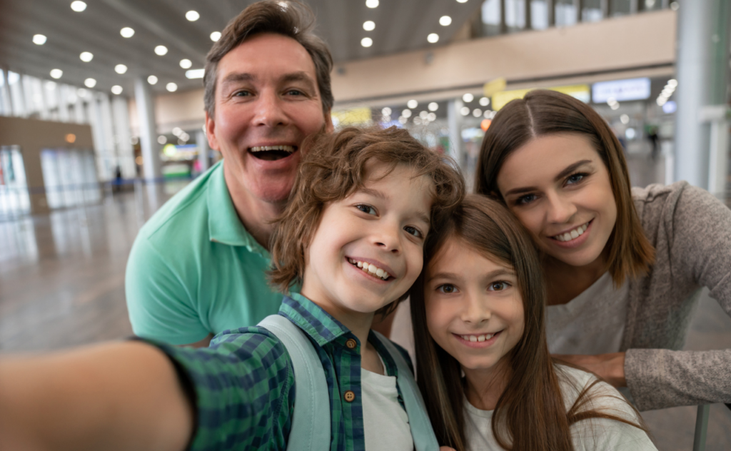 Dark haired family of four smiling as the son takes a selfie at the airport