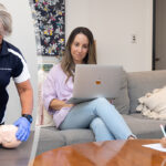 Water safety experts’ launch free training to help families learn to save a life Mum studying online while small boy colours in.