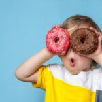 Young boy holding two donuts over his eyes
