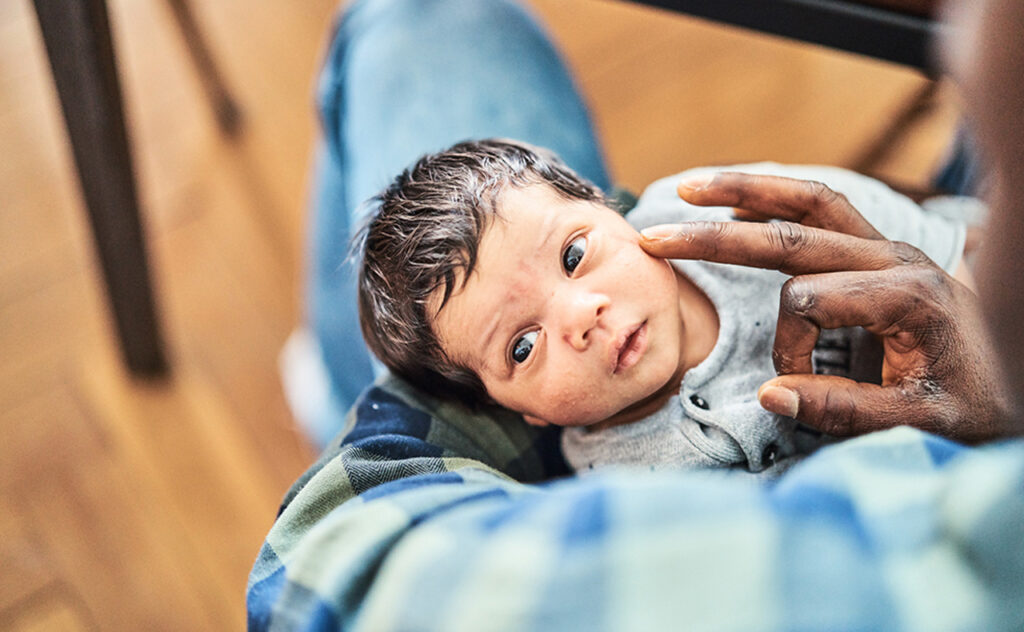 High angle view of cute newborn in father's arms at home. Close-up of a man holding son in living room.