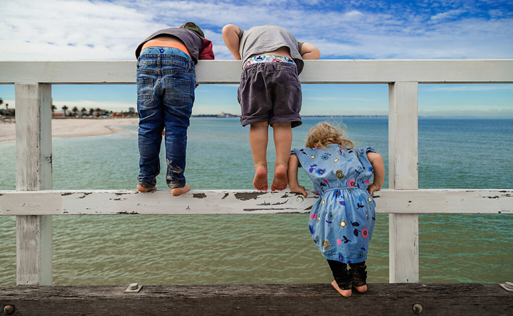 Rear view of siblings looking at sea while standing on railing against sky