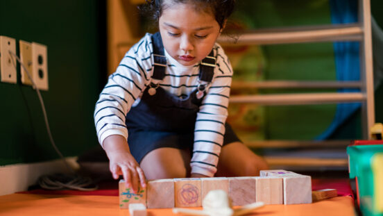 A cute girl with autism spectrum disorder playing and organizing toys by shapes and colors and size. She is 3 and a half years old and focuses her attention on categorizing wooden toys by shapes, colors, and size.