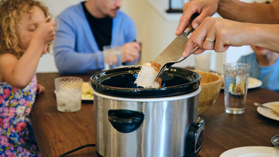 A multiracial family eating dinner in their home. Mum serves dinner from slow cooker.