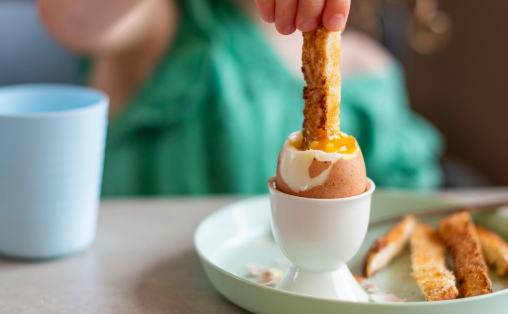 Close up of a finger of toast being dipped into a boiled egg by a child