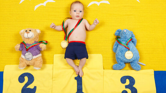 Portrait of a cute child is standing on a place podium in first place. Handsome boy is cheering and standing on victory podium with medal.
