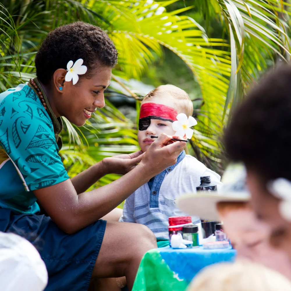 Young boy getting his face painted by beautiful hotel staff at Outrigger Fiji