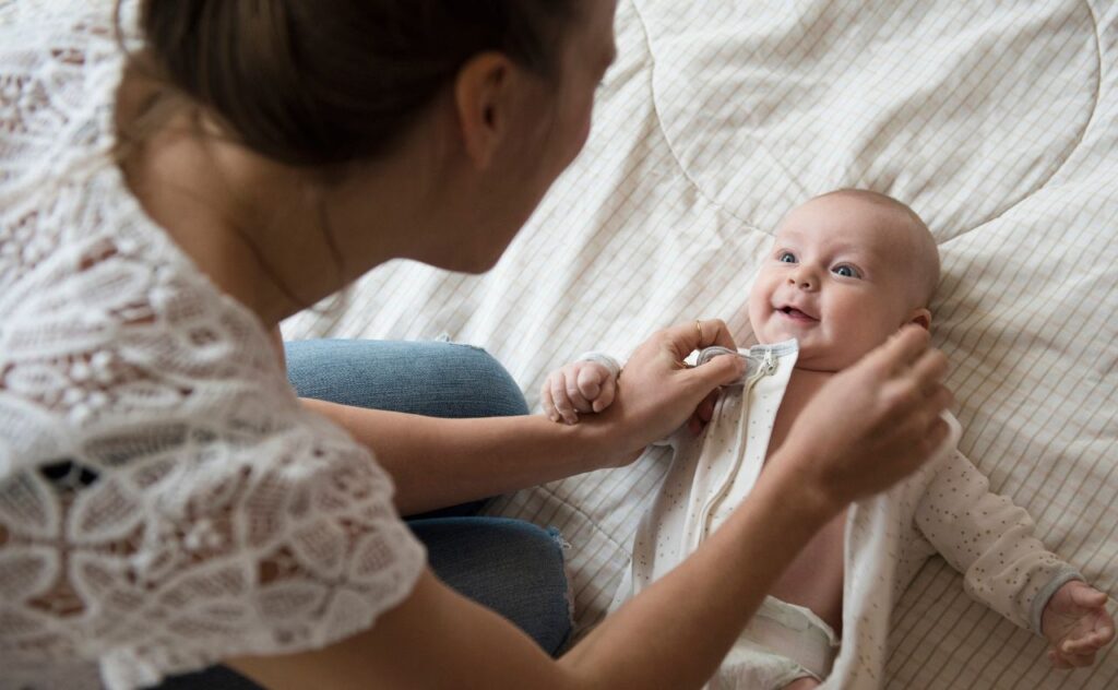 Mother dressing baby on bed