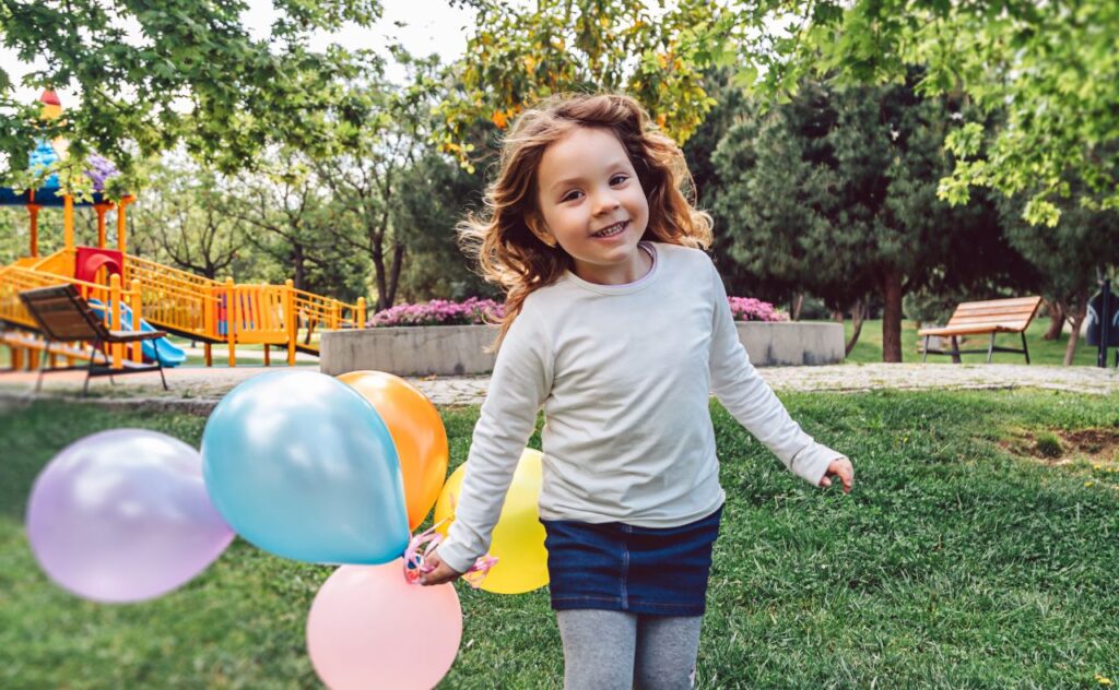 Young girl in a park holding balloons, ready for a party