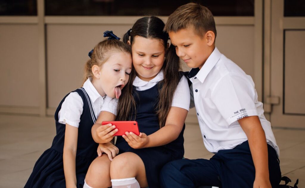 three children in school uniform with a mobile phone