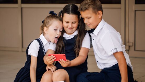 three children in school uniform with a mobile phone