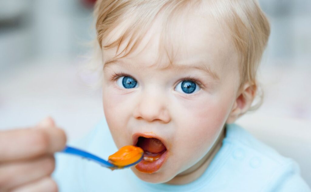 Blue-eyed baby being fed spoonful of food.  